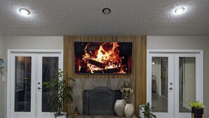 Una sala de estar con chimenea, televisor montado encima y dos puertas.