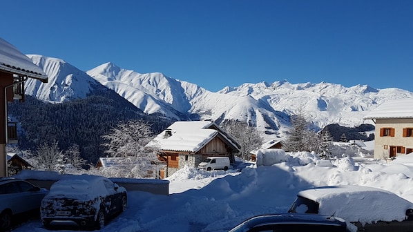 A snow-covered mountain village with traditional wooden houses, a clear blue sky, and a snow-covered car in the foreground.