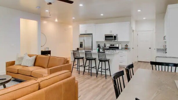 Un salon moderne avec un canapé et une table à manger, une cuisine avec des meubles blancs et un four à micro-ondes, et un ventilateur de plafond.