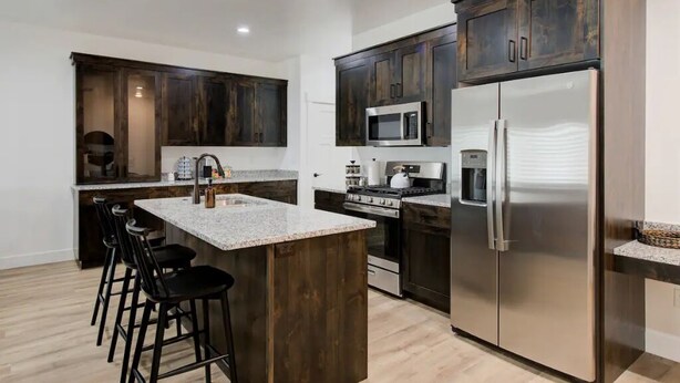 Una cocina moderna con armarios de madera oscura, electrodomésticos de acero inoxidable y una isla central con taburetes de bar.