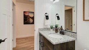 Un baño con lavamanos de encimera de granito, un espejo grande y zona de ducha.