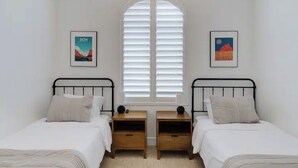 Un dormitorio con dos camas individuales, un ventanal con contraventanas y dos mesitas de noche con lámparas.
