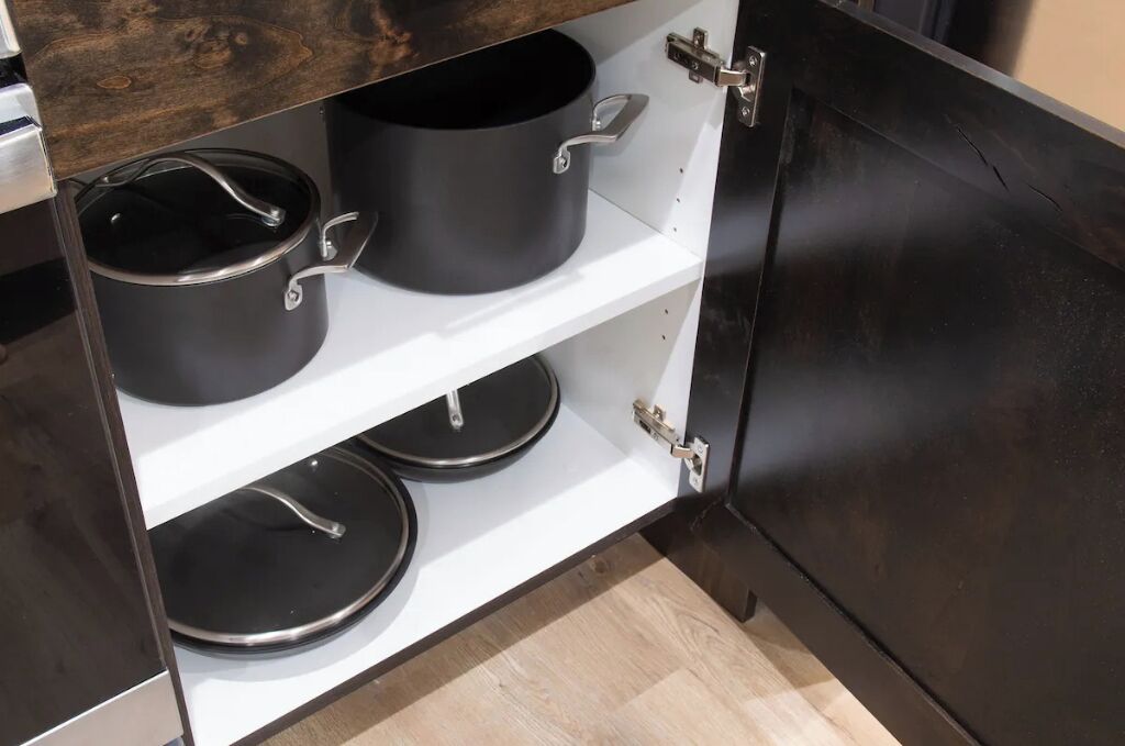 Un meuble de cuisine avec trois casseroles noires posées sur des étagères.