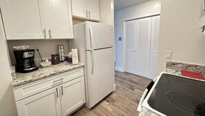 A kitchen with white cabinets, a white refrigerator, a black coffee maker, and a red oven. - Cozy 1 Bedroom Apartment in Downtown Gadsden, AL (Gadsden)