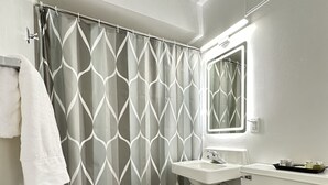 A bathroom with a shower curtain, sink, toilet, and a black mat. - Cozy 1 Bedroom Apartment in Downtown Gadsden, AL (Gadsden)