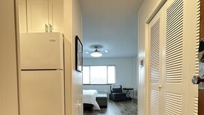 A hallway with a kitchen area, a bedroom with a bed and a window, and a closet with louvered doors. - Cozy 1 Bedroom Apartment in Downtown Gadsden, AL (Gadsden)