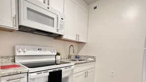 A modern kitchen with white cabinetry, a built-in microwave, a stainless steel sink, and a wood floor. - Cozy 1 Bedroom Apartment in Downtown Gadsden, AL (Gadsden)