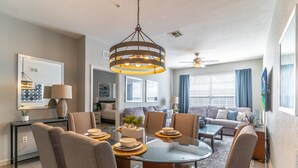 A modern living room with a dining area, featuring a round glass table, comfortable seating, and a unique hanging light fixture. - 2788 Windsor Hills (Kissimmee)