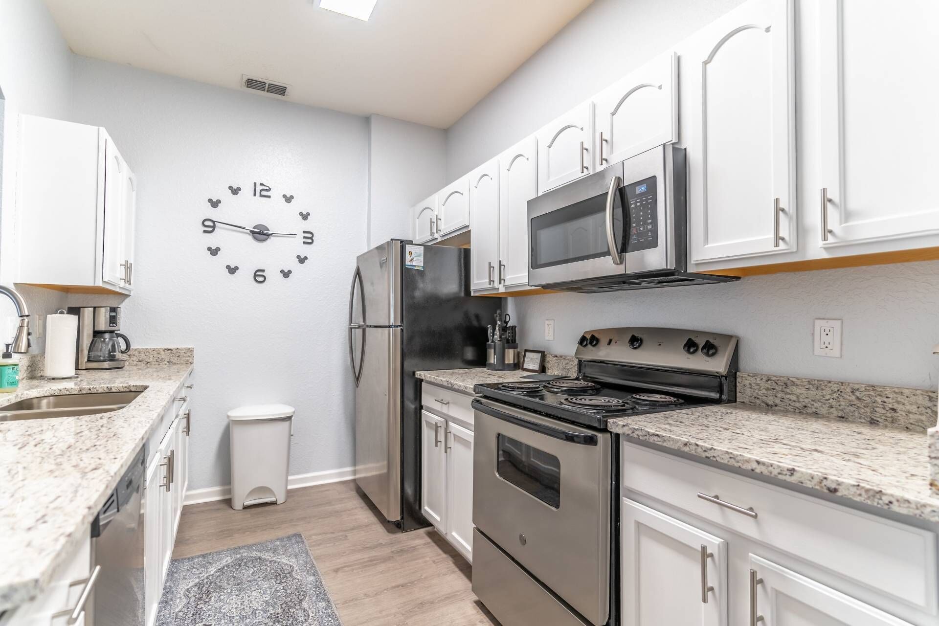A modern kitchen with white cabinets, stainless steel appliances, a microwave, a refrigerator, a stove, and a clock on the wall.