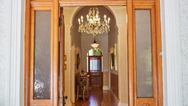 A hallway with a wooden door, a chandelier, and a stained glass window. - VILLA PUCCINI (Cape Town)