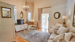 A living room with a sofa, a glass coffee table, a TV, and a chandelier. - VILLA PUCCINI (Cape Town)