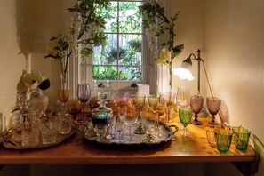 A table with various glassware and a window with a view of greenery. - VILLA PUCCINI (Cape Town)
