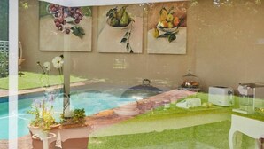 A poolside area with a hot tub, a dining setup with plates and a toaster, and three paintings of fruits on the wall. - VILLA PUCCINI (Cape Town)