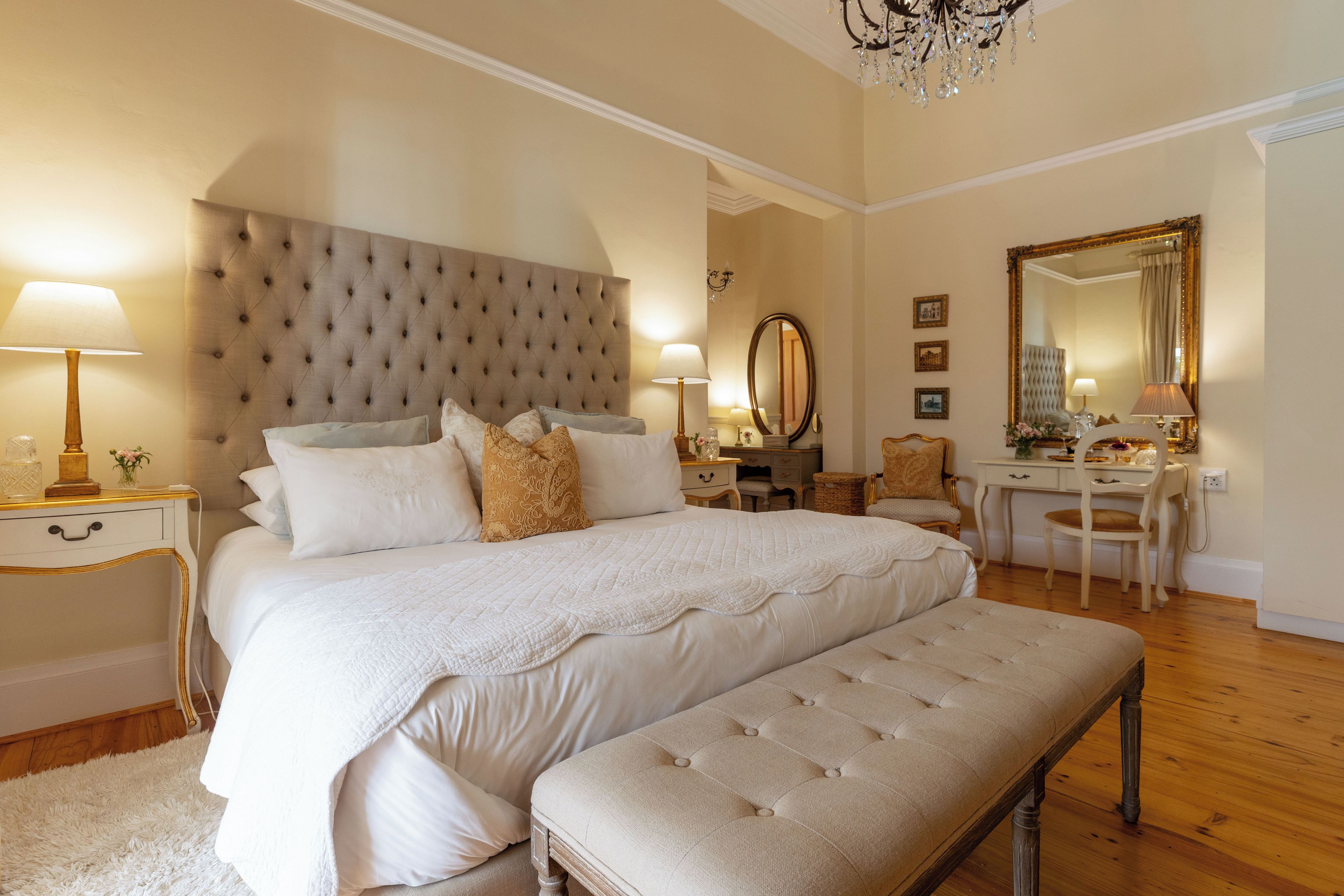 A bedroom with a large bed, bedside tables, a desk, a chair, and a mirror.