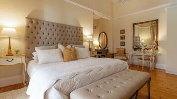 A bedroom with a large bed, bedside tables, a desk, a chair, and a mirror.