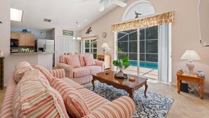 Amplio salón con un sofá grande, una mesa de centro y vista a una piscina a través de puertas de vidrio.