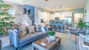 A modern living room with a gray sofa, a coffee table with a plant, and a staircase leading to the kitchen. - 106 Festival (Davenport)
