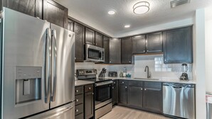 Une cuisine moderne dotée d’appareils électroménagers en acier inoxydable, de meubles de rangement en bois foncé et d’un plancher en bois clair.