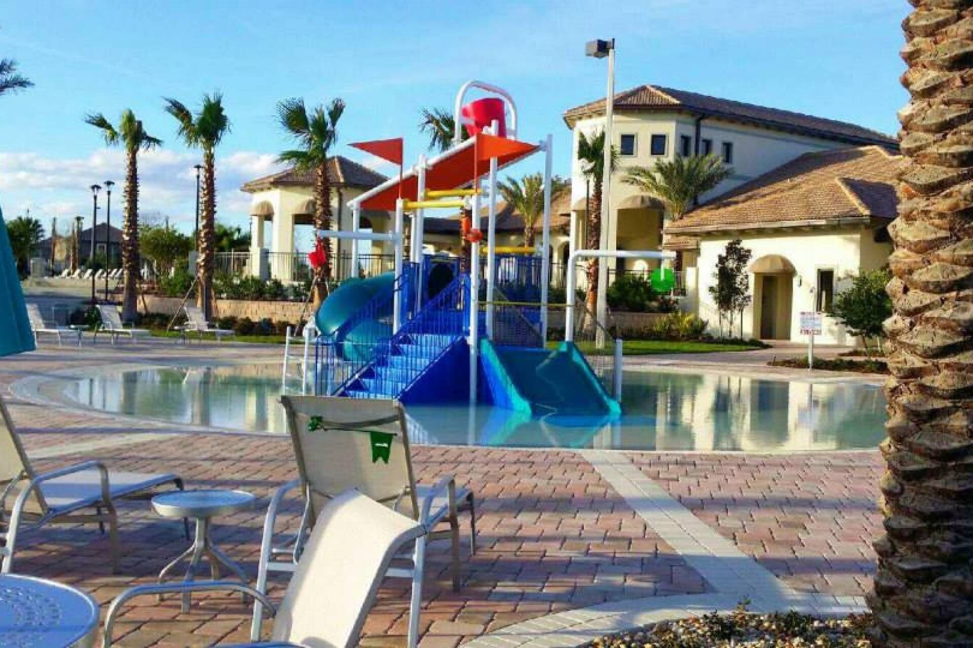 Un espace piscine doté d’un toboggan, de chaises longues et d’un bâtiment dont le toit est recouvert de tuiles.