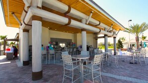 An outdoor patio area with metal chairs and tables, a bar area with a counter and stools, and a covered seating area with a wooden roof. - 1414 Champions Gate (Davenport)