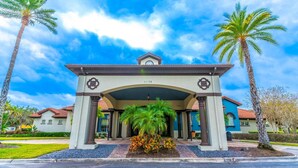 A hotel entrance with a covered walkway, palm trees, and a clear blue sky. - 4552 Bella Vida 2 (Kissimmee)