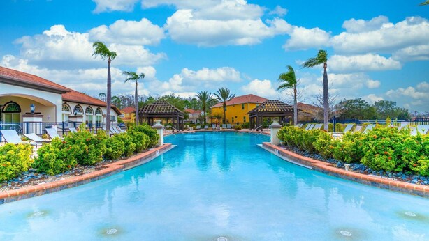 A swimming pool with lounge chairs and palm trees, surrounded by buildings with red roofs. - 4552 Bella Vida 2 (Kissimmee)