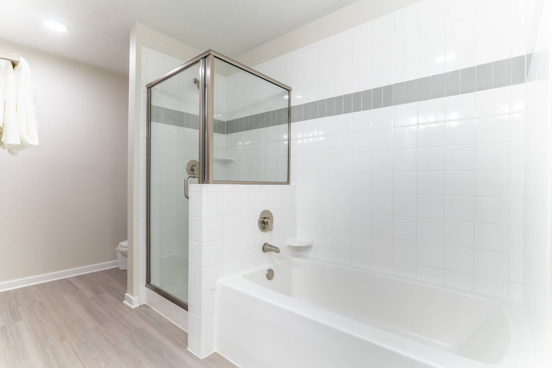 A modern bathroom with a glass-enclosed shower, a white bathtub, and a tiled wall.
