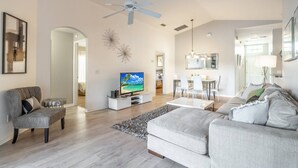 A spacious living room with a grey sofa, a television, and a ceiling fan. - 17637 Silver Creek (Clermont)