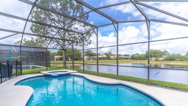 A swimming pool with a curved edge, surrounded by a metal fence, and a view of a lake and houses in the background. - 17637 Silver Creek (Clermont)