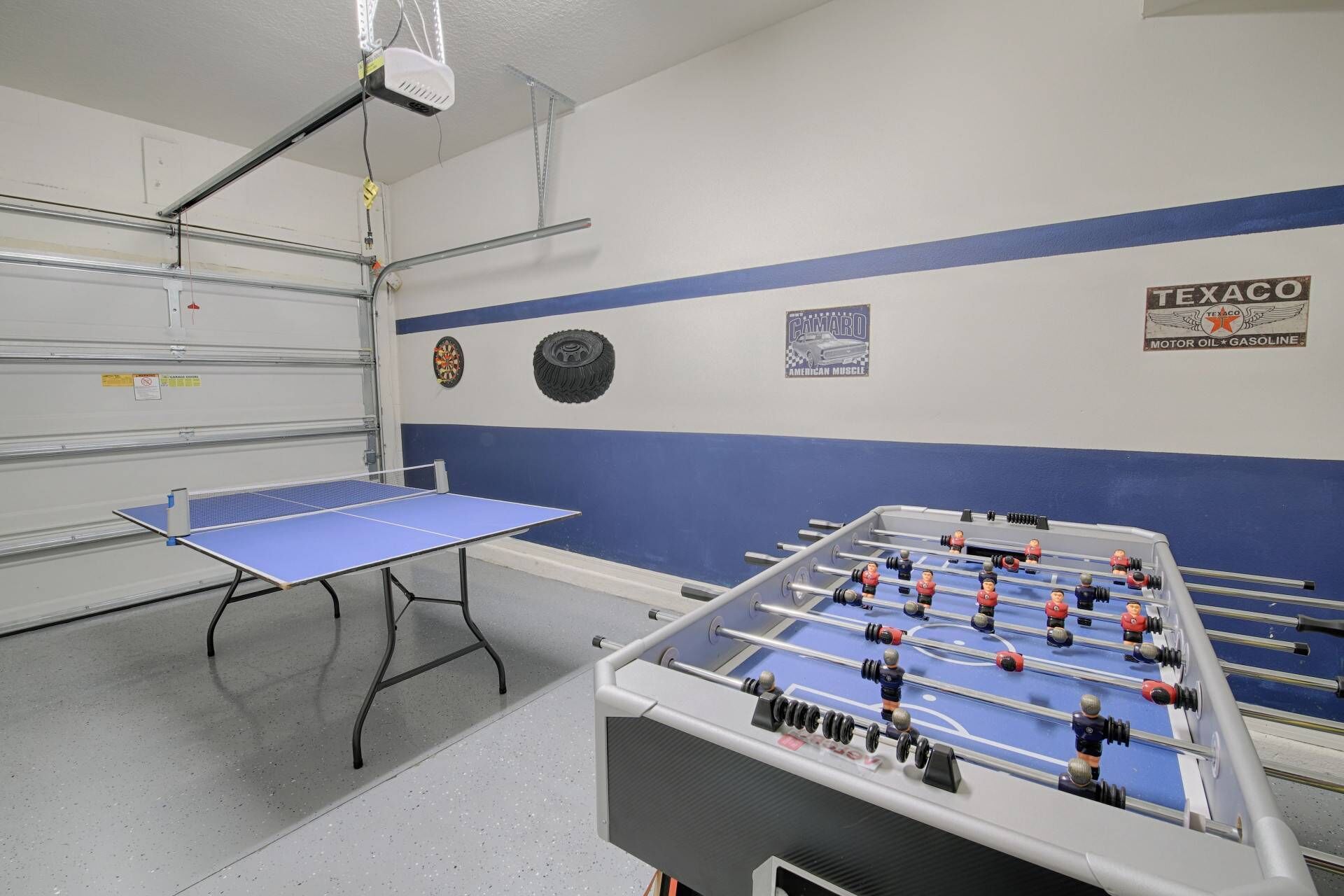 Una stanza con un tavolo da calcio balilla, un tavolo da ping pong e un proiettore a parete.
