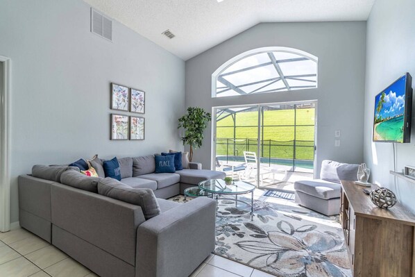 Relax in this stylish living room with a sofa, armchair, and flat-screen TV, offering a view of the beautifully manicured lawn.