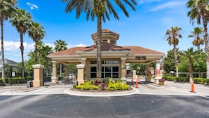 A hotel entrance with a covered area, palm trees, and a gated driveway. - 7755 Windsor Hills (Kissimmee)
