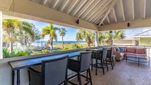A covered outdoor seating area with a view of the beach and palm trees.