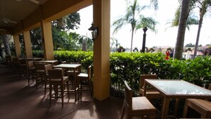 An outdoor cafe area with wicker furniture and glass tables, surrounded by lush greenery and palm trees. - 3088 Encantada (Kissimmee)