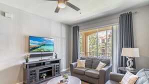 A living room with a flat-screen TV, a grey sofa, a coffee table, and a ceiling fan. - 2821 Windsor Hills (Kissimmee)