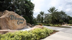 A large rock with "Discovery Cove" written on it, surrounded by lush greenery and palm trees. - 2821 Windsor Hills (Kissimmee)