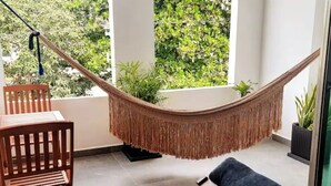 Eine Hängematze, die zwischen zwei Fenstern gespannt ist, mit einem Holztisch und Stühlen sowie einem blauen Sofa in einem hellen Raum mit Pflanzen.