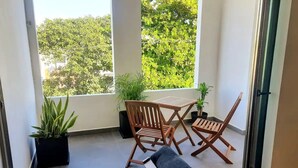 Ein Balkon mit Holztisch und Stühlen, zwei Blumentöpfen und einem grauen Sofa.