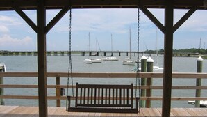 A wooden deck with a swing overlooking a marina with boats and a bridge in the background. - Stunning River Views-Easy Walk to Beach & Shops-Pool and Day dock!-3BR Townhome (Folly Beach)