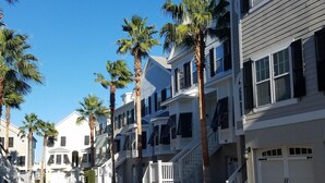 A row of white multi-story buildings with balconies, palm trees, and a clear blue sky. - Stunning River Views-Easy Walk to Beach & Shops-Pool and Day dock!-3BR Townhome (Folly Beach)