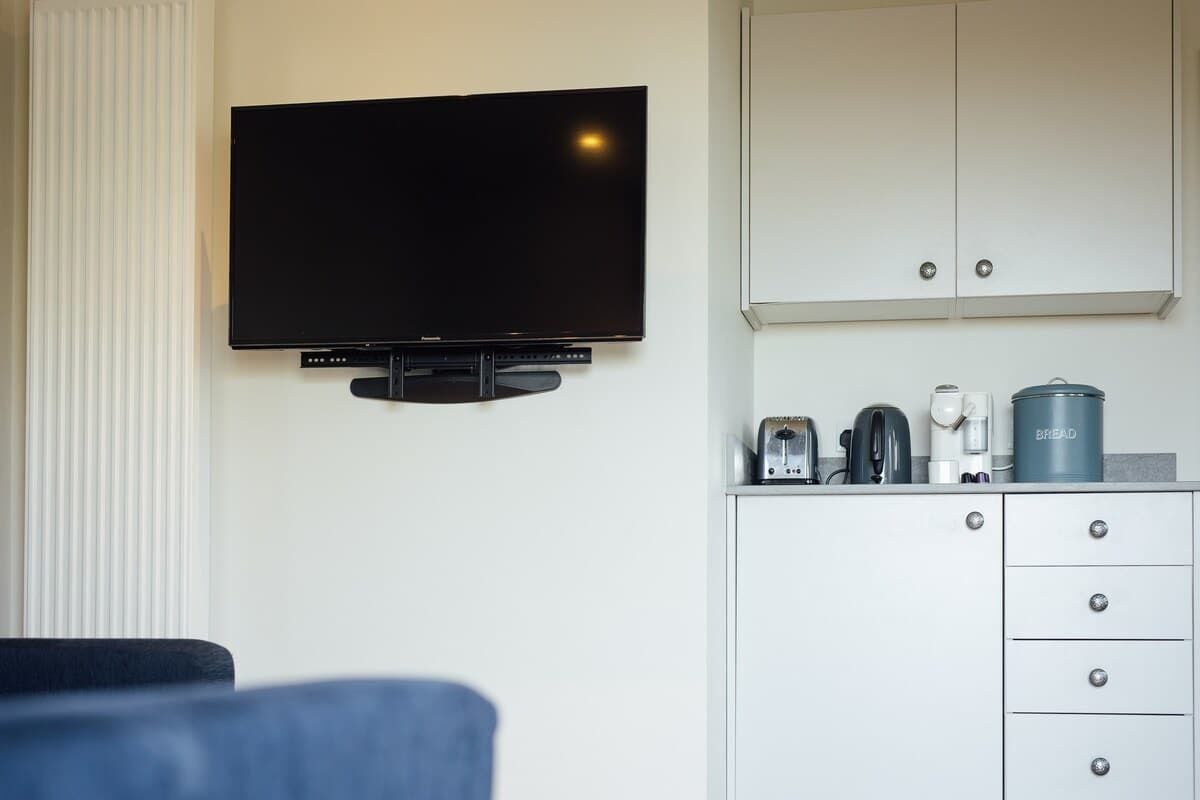 Une chambre moderne dotée d’un téléviseur à écran plat fixé au mur, d’une armoire blanche avec des tiroirs et d’une machine à café posée sur le comptoir.
