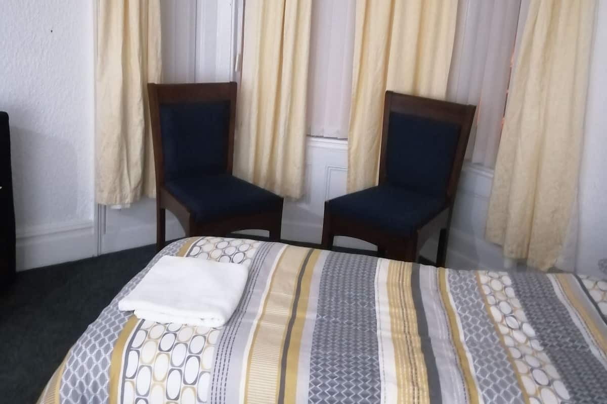 A hotel room with a bed, two chairs, and curtains.