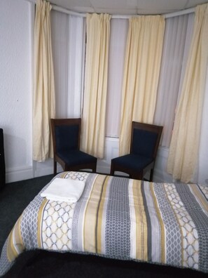 Una habitación de hotel con cama, dos sillas y cortinas.