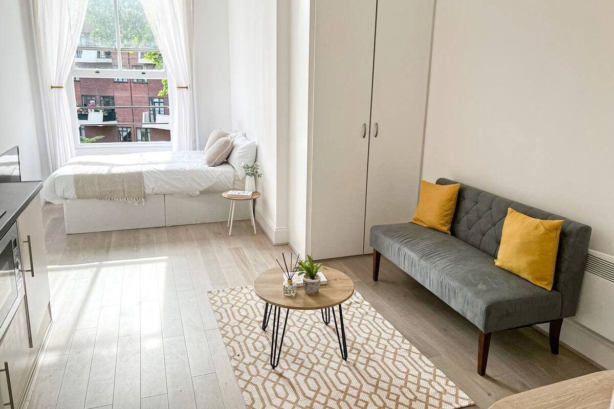 Une chambre à coucher moderne avec un lit, un canapé gris, une petite table ronde et une armoire.