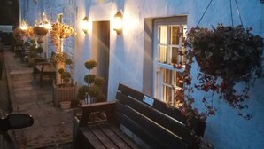 Un edificio con mesas al aire libre, un banco y plantas colgantes.