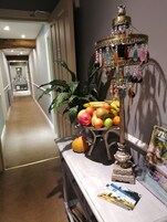 Um corredor decorado com um suporte de frutas, um vaso de plantas e um quadro sobre uma mesa.