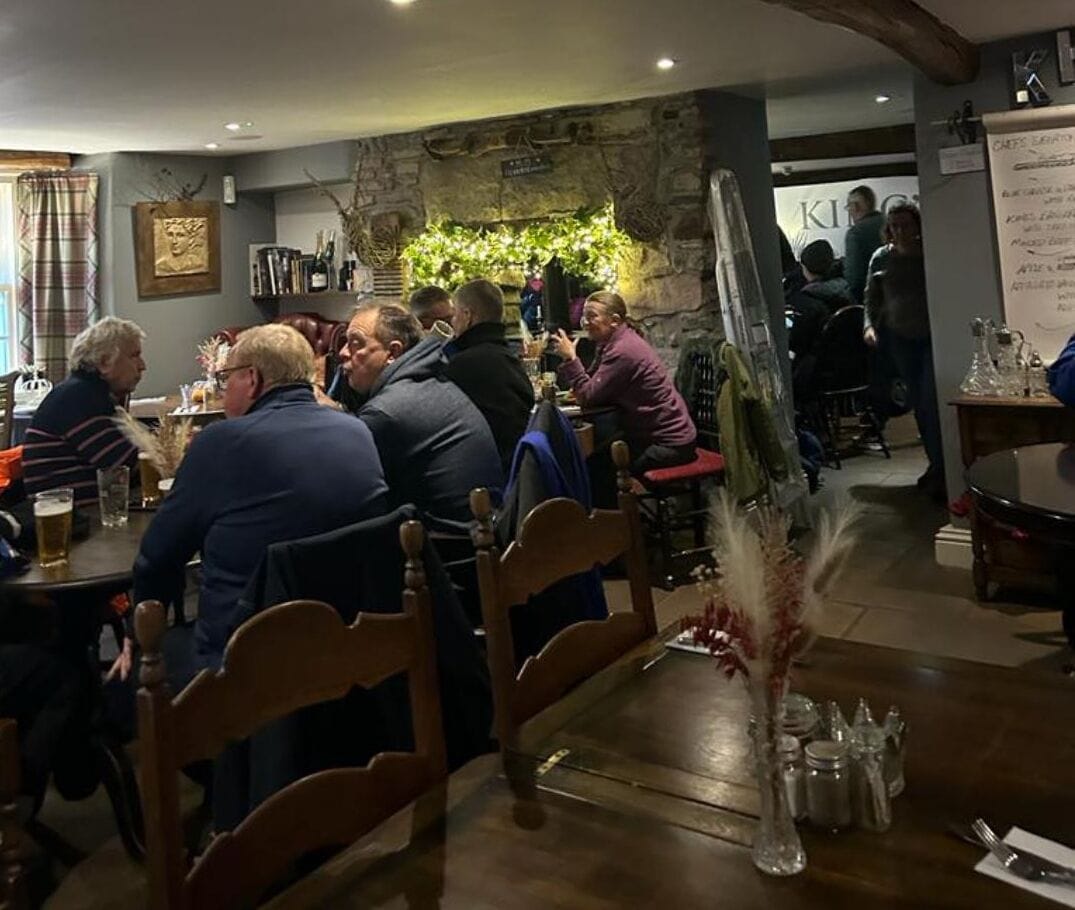 Interior de restaurante con mesas y sillas de madera, y un fondo de pared de piedra.