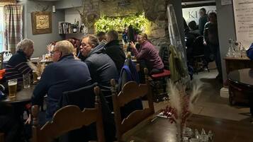 Interior de restaurante con mesas y sillas de madera, y un fondo de pared de piedra.