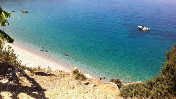 A coastal view with clear turquoise waters, a sandy beach, and a boat in the distance.