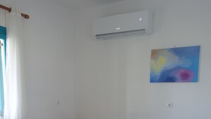 A room with a dining table, chairs, a sofa, an air conditioning unit, and a wall-mounted painting.